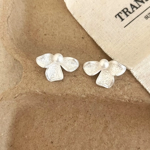 Macro shot of silver textured flower earrings with white pearl center on eco-pulp tray