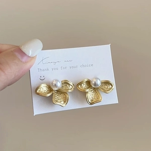 Textured gold flower petal earrings with white pearl center on elegant display card