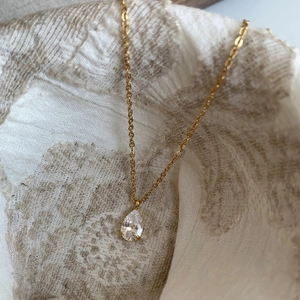 Elegante collana dorata con pendente in zirconia a goccia su sfondo in pizzo raffinato