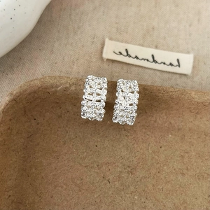 Detailed macro view of silver textured rectangular hoop earrings on a vintage display box