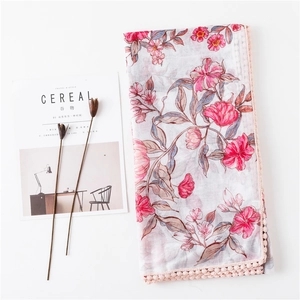 Détail macro d'une écharpe en coton et lin gris avec imprimé floral et bordure à pompons