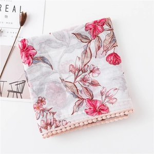 Détail d'une écharpe en lin à fleurs avec bordure à pompons roses et motif floral