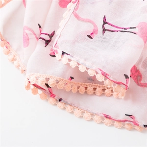 Détail d'une écharpe en coton et lin rose avec imprimé flamant rose et pompons