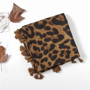 Détail d'une écharpe imprimé léopard avec glands sur fond blanc et feuilles d'automne