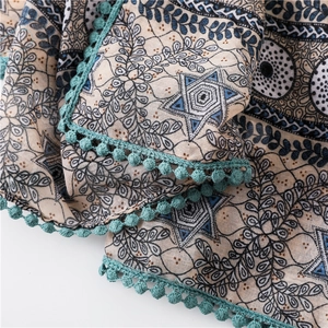 Détail d'une écharpe bohème aux motifs d'étoiles bleues et bordure à pompons turquoise