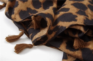 Détail d'une écharpe léopard montrant les glands bruns et la texture tissée douce