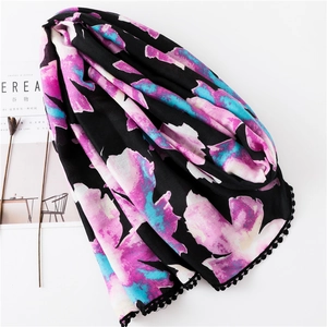 Détail de l'écharpe en lin et coton noir avec imprimé fleuri et bordure de pompons déco