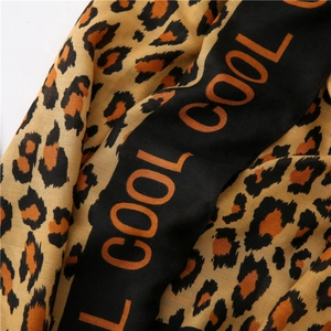 Macro detail of leopard print scarf featuring orange COOL lettering and twill fabric texture