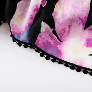 Détail d'une écharpe en lin à imprimé floral avec pompons noirs et texture de tissu