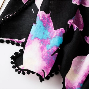 Détail d'une écharpe fleurie avec pompons noirs et motifs de fleurs abstraites roses