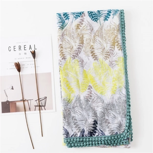Détail d'écharpe bohème avec imprimé plumes et bordure pompon sur fond blanc