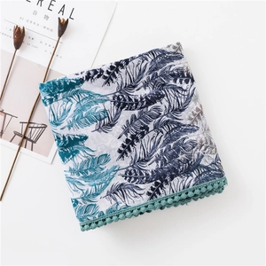 Détail d'une écharpe bohème avec imprimé plumes et bordure pompon turquoise sur fond blanc