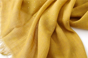 Detailed texture of ginger yellow cotton scarf with silver rhinestones and fringe edges