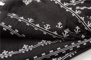 Detailed macro view of black cotton-linen fabric with white cross-stitch embroidery patterns