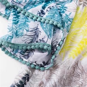 Détail d'une écharpe à imprimé plumes colorées avec bordure pompon et tissu doux