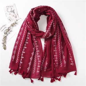 Detailed close-up of dark red linen scarf featuring white embroidery and tassel trim