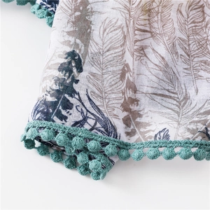 Détail d'une écharpe en coton blanc avec motif plumes et bordure à pompons turquoise