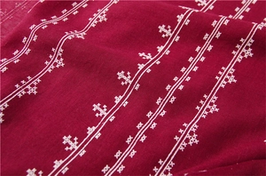 Macro detail of dark red linen scarf featuring white cross-stitch geometric patterns