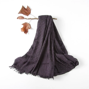 Detail of dark purple cotton linen scarf with white polka dots and fringed edges on branch