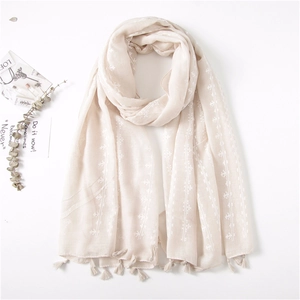 Detail of light beige cotton linen scarf with embroidery and tassels on white background