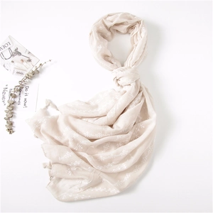 Detailed close-up of light beige linen scarf featuring white floral patterns and tassels
