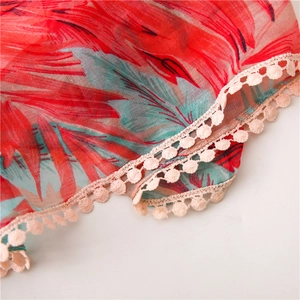 Détail d'une écharpe en coton et lin à fleurs rouges avec bordure en pompons beige