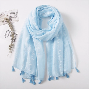 Detail of light blue cotton linen scarf with white star embroidery and fringe tassels