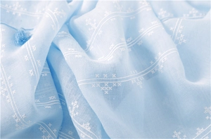 Close-up of light blue cotton linen scarf with white geometric embroidery and tassels