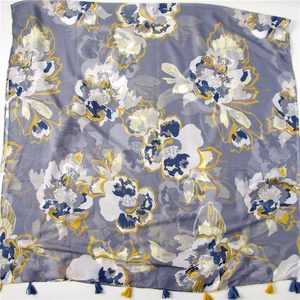 Detail of floral printed gray linen shawl with blue and yellow tassels on white background