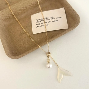 Détail du collier doré avec perle et pendentif queue de poisson en nacre sur plateau