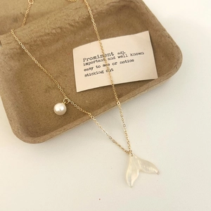 Détail d'un collier en chaîne dorée avec une perle blanche et un pendentif queue de poisson