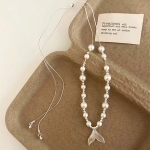 Close-up of shell fishtail pendant necklace with white pearls on a minimalist tray