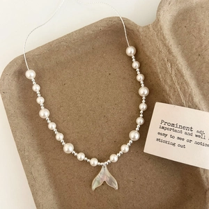 Detailed view of pearl necklace with shell fishtail pendant on a textured paper tray