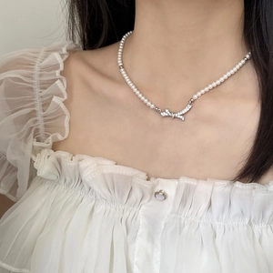 Collier de perles élégant avec pendentif nœud serti de zircons porté par un mannequin