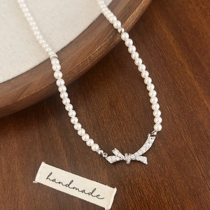Gros plan d'un collier de perles avec pendentif nœud serti de cristaux sur bois sombre