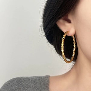 Close-up of gold hoop earrings with faceted geometric texture on female model