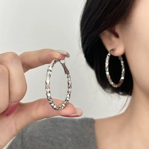Detail of silver large hoop earrings featuring a geometric faceted diamond-cut texture