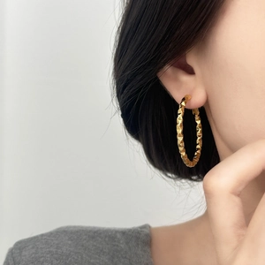 Close-up of a large gold hoop earring with geometric diamond-cut texture on female model