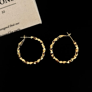 Detail of large gold hoop earrings with textured geometric surface on black background