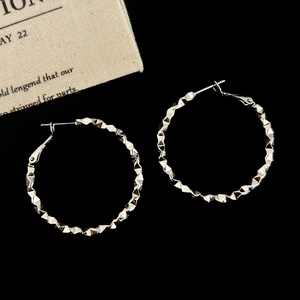 Macro shot of silver hoop earrings with geometric faceted texture on a black backdrop