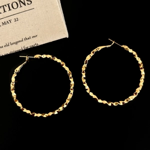 Macro detail of large gold-plated hoop earrings featuring a faceted hammered texture finish