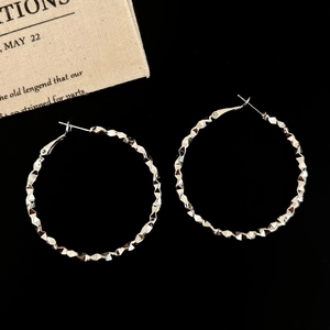 Macro shot of silver textured hoop earrings with geometric faceted design on dark backdrop