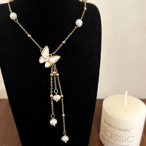 Elegant gold butterfly necklace with freshwater pearls and shell tassels on a display stand