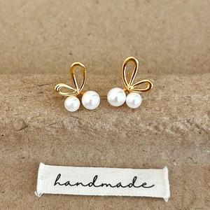 Detail of handmade gold butterfly pearl earrings on a rustic brown paper background