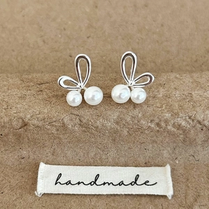 Detail view of silver metal bunny ear earrings with white pearls on handmade label