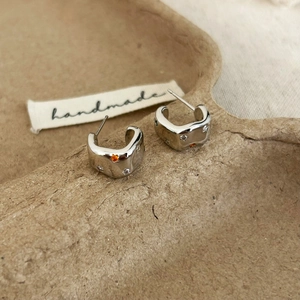 Détail de boucles d'oreilles argentées en C avec zircons colorés sur un plateau en papier