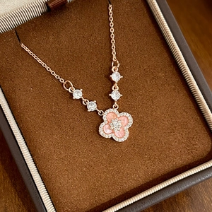 Gros plan d'un collier trèfle à quatre feuilles or rose avec nacre rose et zircons