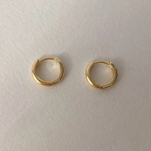 Close-up of minimalist gold hoop earrings with a polished mirror finish on a grey surface