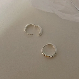 Close-up of polished silver geometric hoop earrings on a minimalist grey surface