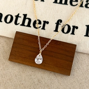 Elegant gold chain necklace with a clear teardrop zircon pendant on a rustic wood block